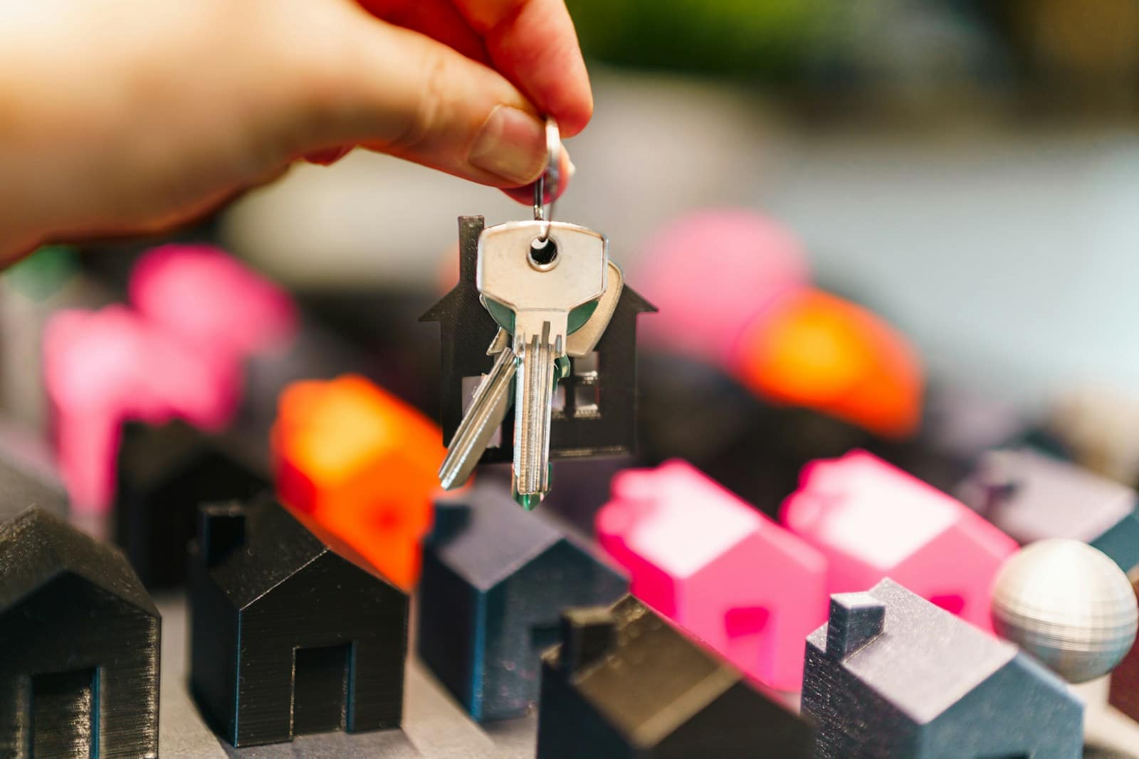 A hand holding house keys above a row of miniature houses